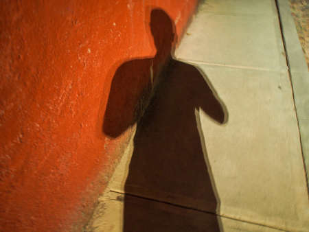 Shadow, of a torso,  red wall and cement sidewalk at night, contrasting colors and shapes.の写真素材