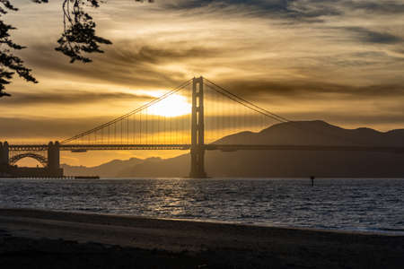 Sunset alongside the north tower of the Golden Gate Bridge with a gold yellow skyの写真素材
