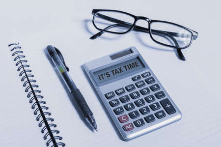 Tax day text written on calculator next to a pen and glasses on top of a notebook.の写真素材