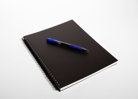 Blue pen on top of a black notebook against a white backgroundの写真素材