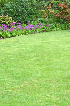 A perfectly manicured country garden in the english style with a sweeping pristine lawn edged with a beautiful border filled with colourful plants, shrubs and small trees. Simply perfect.の写真素材