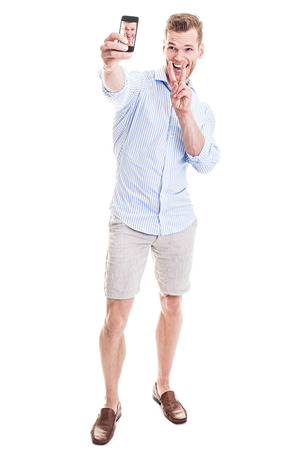 Full length portrait of a happy young man showing a peace sign and taking a SELFIE - isolated on whiteの写真素材