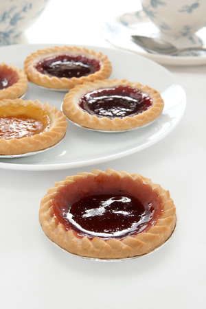 Jam tarts and afternoon tea on a white table clothの写真素材