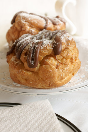 Choux buns filled with cream and drizzled with chocolate and icing sugar