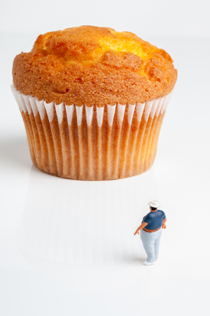 Overweight man looking up at an enormous muffin a portion size or obesity conceptの写真素材