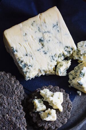 Mature English Stilton cheese with charcoal crackers on a pewter plate shot with low key lightの写真素材