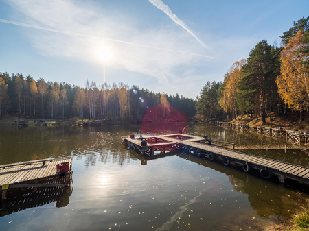 Lake with a pier and places for recreation, surrounded by autumn forestの写真素材