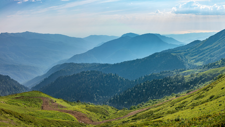 The view from the height of a green mountain valley with residential buildings surrounded by high mountains. Snow-capped mountain peaks on the horizon.の写真素材