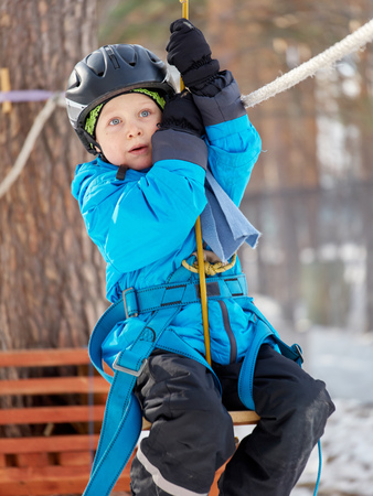 A little boy (6 years old) mountaineering in the winter in a children's rope town, The boy rides a cable trolleyの写真素材