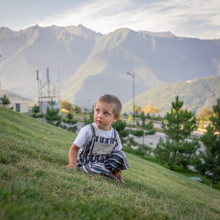 A little boy sitting on a green slope amidst the mountainsの写真素材