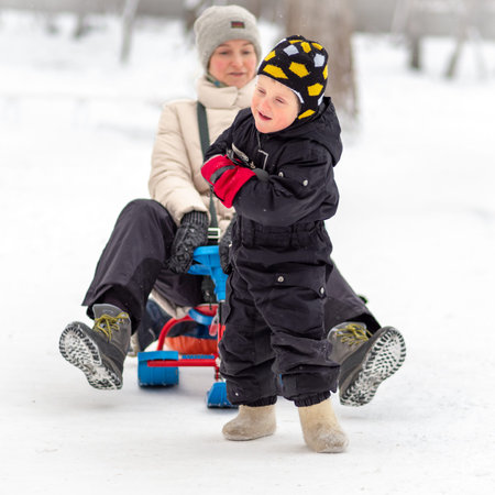 Strong little boy in felt boots carries her mother on a sled.