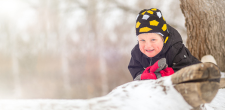 A little boy in felt boots sits on a large fallen tree in winterの写真素材