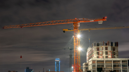 Tower cranes at a construction site in the night city. Electric light with rays.の写真素材