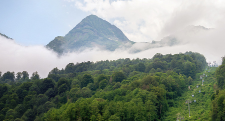 Spectacular panoramic view of green mountains with cable car and peaks in dense fog. Black Pyramid Mountain, Krasnaya Polyana, Sochi, Caucasus, Russiaの写真素材
