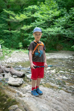 A boy traveler with a backpack and trekking sticks passes the stream fordの写真素材