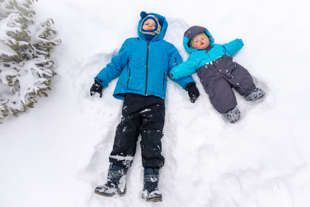 Two boys, 8 and 0 years old, lie in a clean white snowdrift near the spruce. Copy space backgroundの写真素材
