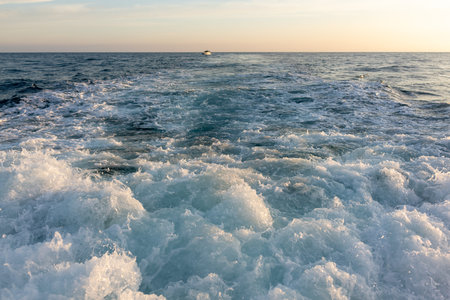Powerful waves and foam astern of the yacht when moving during sunsetの写真素材