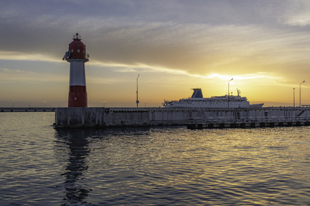 Lighthouse and cruise liner docked in the port, illuminated by the beautiful orange sunset sun. Background with copy spaceの写真素材