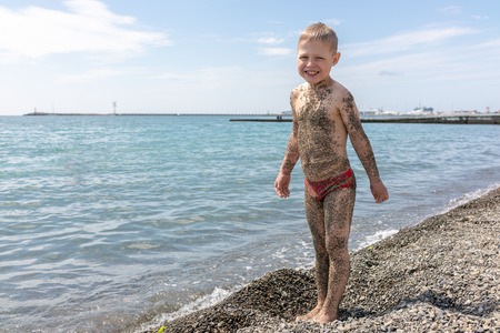 The boy is covered with small pebbles after lying on the beach on a sunny day.の写真素材