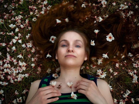 The girl is lying on the grass, strewn with white and pink flowers. The girl is resting on the grass. Flowers in the girls hair.の写真素材