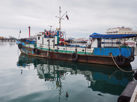 Old rusty fishing boat docked in port in cloudy dayの写真素材