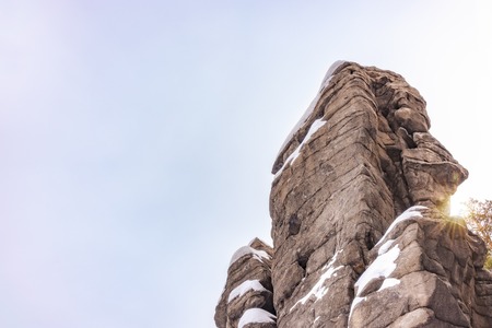 Granite layered rocks covered with snow against the blue sky. The sun looks out from behind the rock.の写真素材