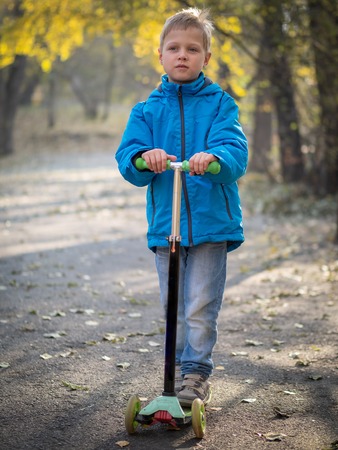 A boy in blue clothes riding a scooter in the autumn park.の写真素材