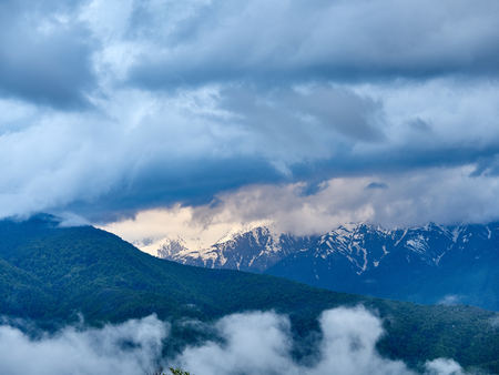 Green forest on the background of high snowy mountains. Spring colors. Snowy mountains in the fogの写真素材