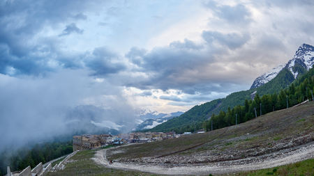 Ski resort in the spring against the backdrop of snowy mountains on a cloudy day. Snowy mountains in the fog. Krasnaya Polyana, Sochi, Russiaの写真素材