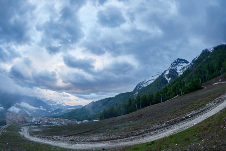 Ski resort in the spring against the backdrop of snowy mountains on a cloudy day. Snowy mountains in the fog. Krasnaya Polyana, Sochi, Russiaの写真素材