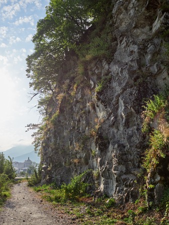Steep cliff with trees growing on it in the light of the setting sun. Hiking trail next to the cliff. Hotel complex ahead.の写真素材