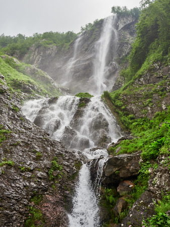Views of the green mountains with rocks and the highest waterfall. Powerful stream of a mountain river among stones and rocks.の写真素材