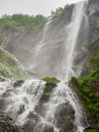 Views of the green mountains with rocks and the highest waterfall. Powerful stream of a mountain river among stones and rocks.の写真素材
