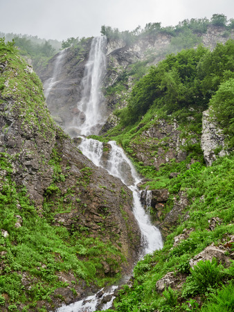 Views of the green mountains with rocks and the highest waterfall. Powerful stream of a mountain river among stones and rocks.の写真素材
