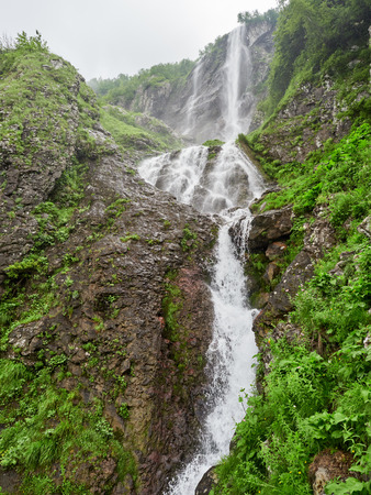 Views of the green mountains with rocks and the highest waterfall. Powerful stream of a mountain river among stones and rocks.の写真素材