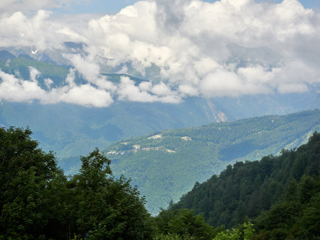 Green mountain slope with serpentine road that descends into the valley. Thick clouds over the mountainsの写真素材