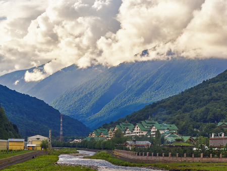 The river flows between the green mountains in front of the complex. High mountains with peaks in the clouds.の写真素材