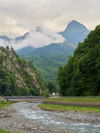 A small river between the green mountains. High mountains with ski slopes in the distance. Summer in the mountains. High green mountains with peaks in thick cloudsの写真素材
