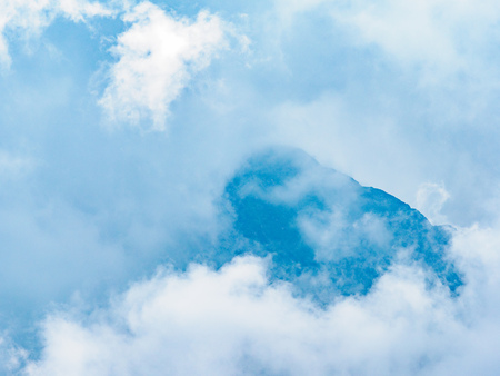 High mountain with green slopes hidden in thick clouds and fog. Heavy fog in the mountains on a cloudy day.の写真素材