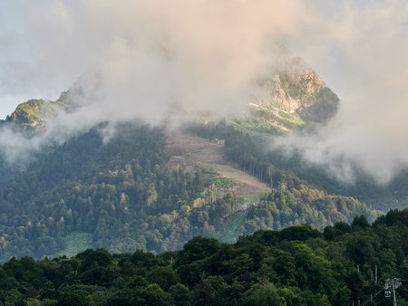 Green mountain slope with cable cars and ski runs at overcast summer sunset. Black Pyramid Mountain, Krasnaya Polyana, Sochi, Caucasus, Russiaの写真素材