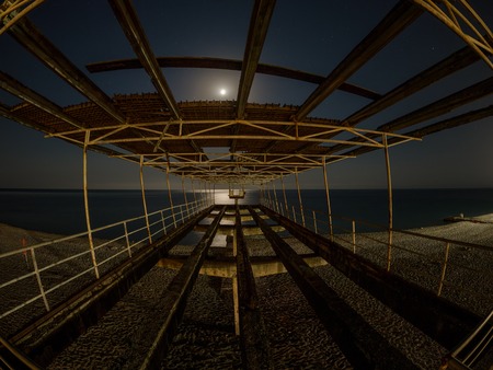 Remains of a destroyed old concrete pier on the seashore at night by the light of the moon.の写真素材