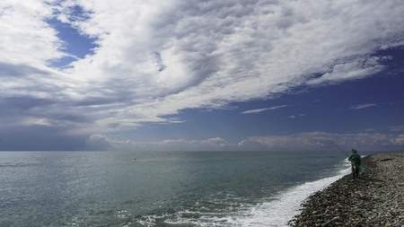 Fisherman with a fishing rod on the sea shore on a cloudy rainy dayの写真素材