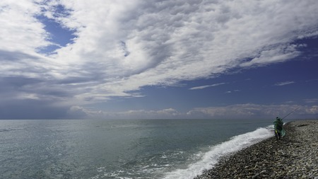 Fisherman with a fishing rod on the sea shore on a cloudy rainy dayの写真素材