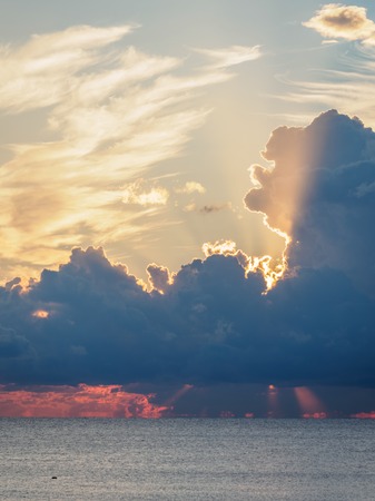 Beautiful yellow-pink sunset in the clouds over the sea. The rays of the setting sun pass through the clouds. The sun disappeared behind the clouds.の写真素材
