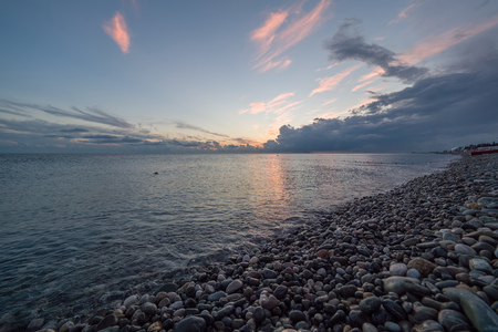 A beautiful pink sunset on a pebble beach. The rays of the setting sun pass through the clouds. The sun disappeared over the sea.の写真素材