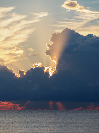 Beautiful yellow-pink sunset in the clouds over the sea. The rays of the setting sun pass through the clouds. The sun disappeared behind the clouds.の写真素材