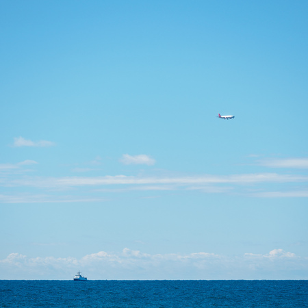 Calm sea and clear blue sky. The lonely ship is far away on the horizon and the plane approaching the landing. Copy space backgroundの写真素材