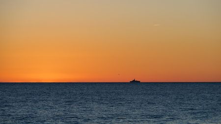 Orange sunset over the sea. Lonely ship on the horizon. The sun hides behind the horizon in the sea.の写真素材