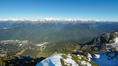 Panoramic view from the top of the Aibga mountain range to the ski resort Rosa Khutor. The valley is surrounded by high mountains with snowy slopes. Krasnaya Polyana, Sochi, Caucasus, Russia.の写真素材
