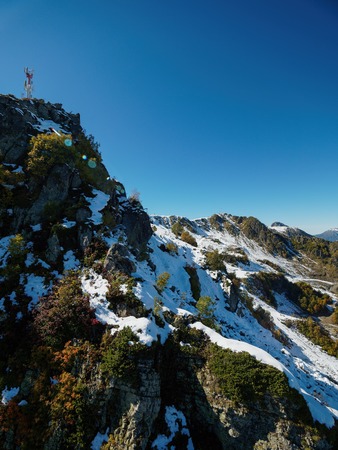 Snowy mountain peak with green and yellow trees. Clear blue sky.の写真素材